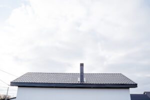 A white building with a dark, energy-efficient roofing and a central chimney stands against a cloudy sky. Only the upper part is visible, highlighting modern roofing options beneath the vast expanse of sky above.